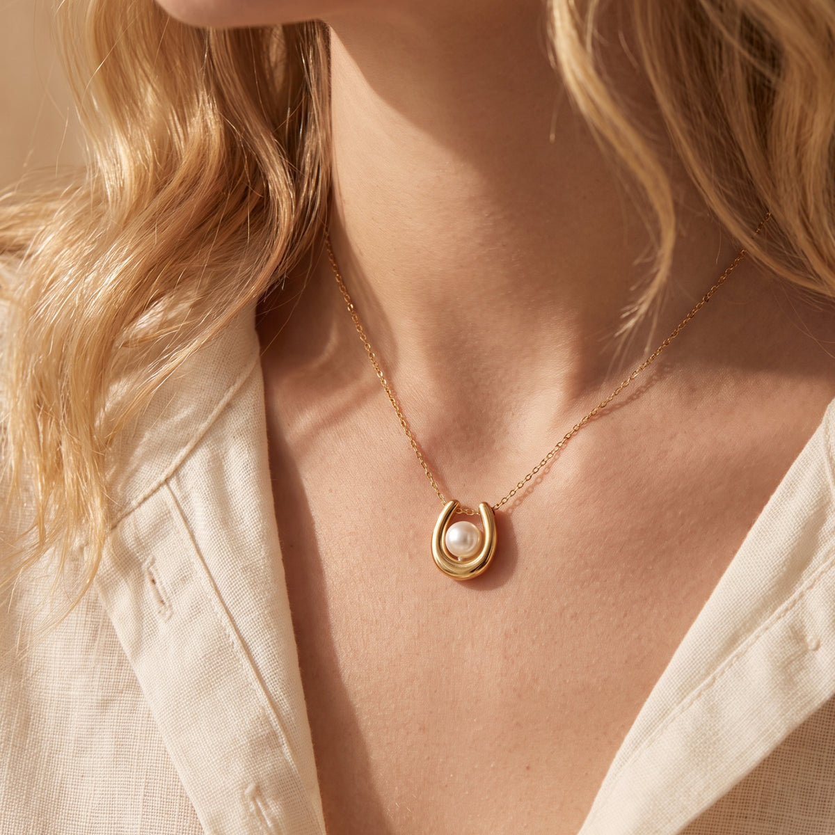 Close-up of a model wearing the gold-tone horseshoe necklace with a centered white pearl.