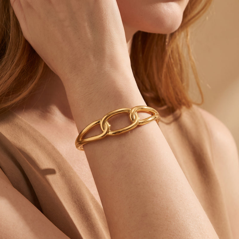 Close-up of a model wearing the gold-tone sculptural link cuff bracelet on her wrist.