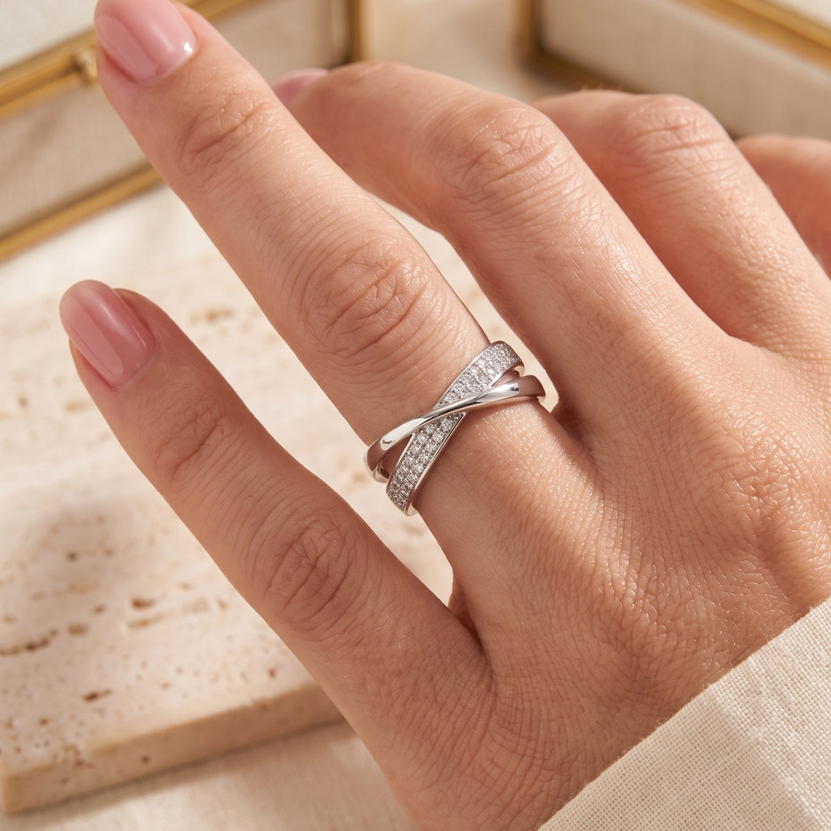 Silver intertwined crossover ring with pavé stones worn on a finger.