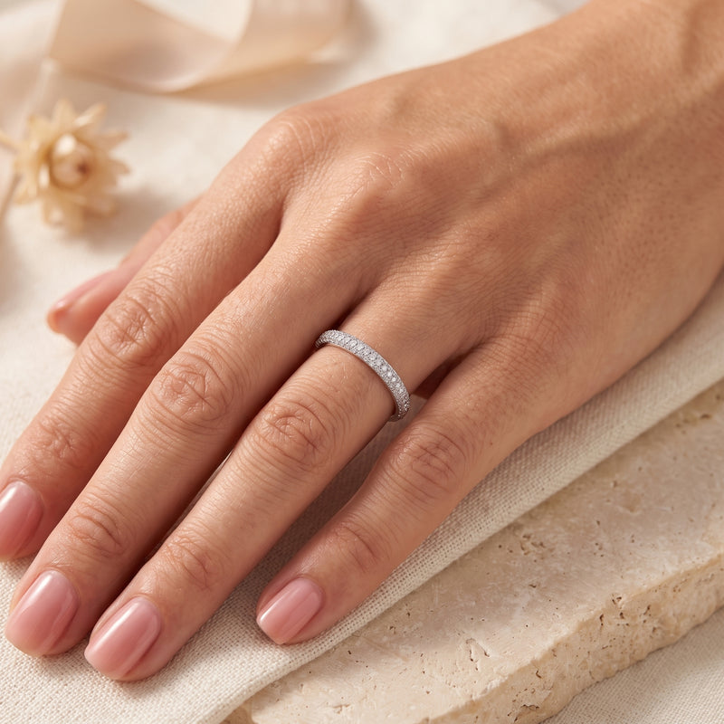 Silver multi-row pavé band ring worn on a hand over cream fabric and a beige stone block.
