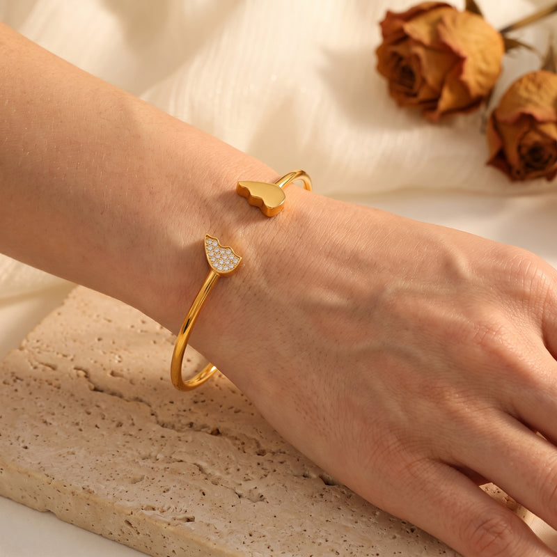Close-up of a wrist wearing the gold-tone broken-heart cuff bracelet with smooth and crystal-accented halves.