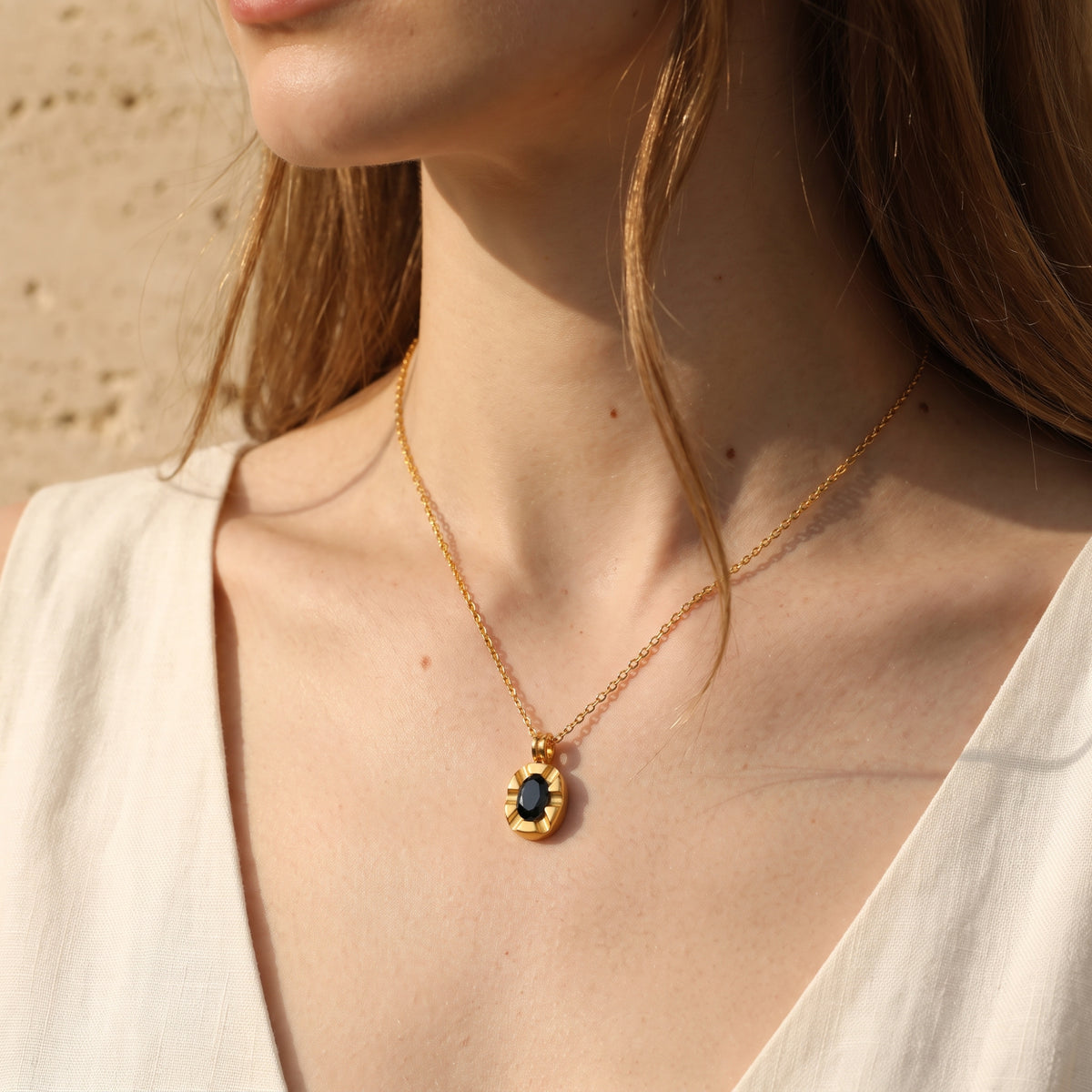 Model wearing the fluted gold oval medallion necklace with a black stone center over a white top.