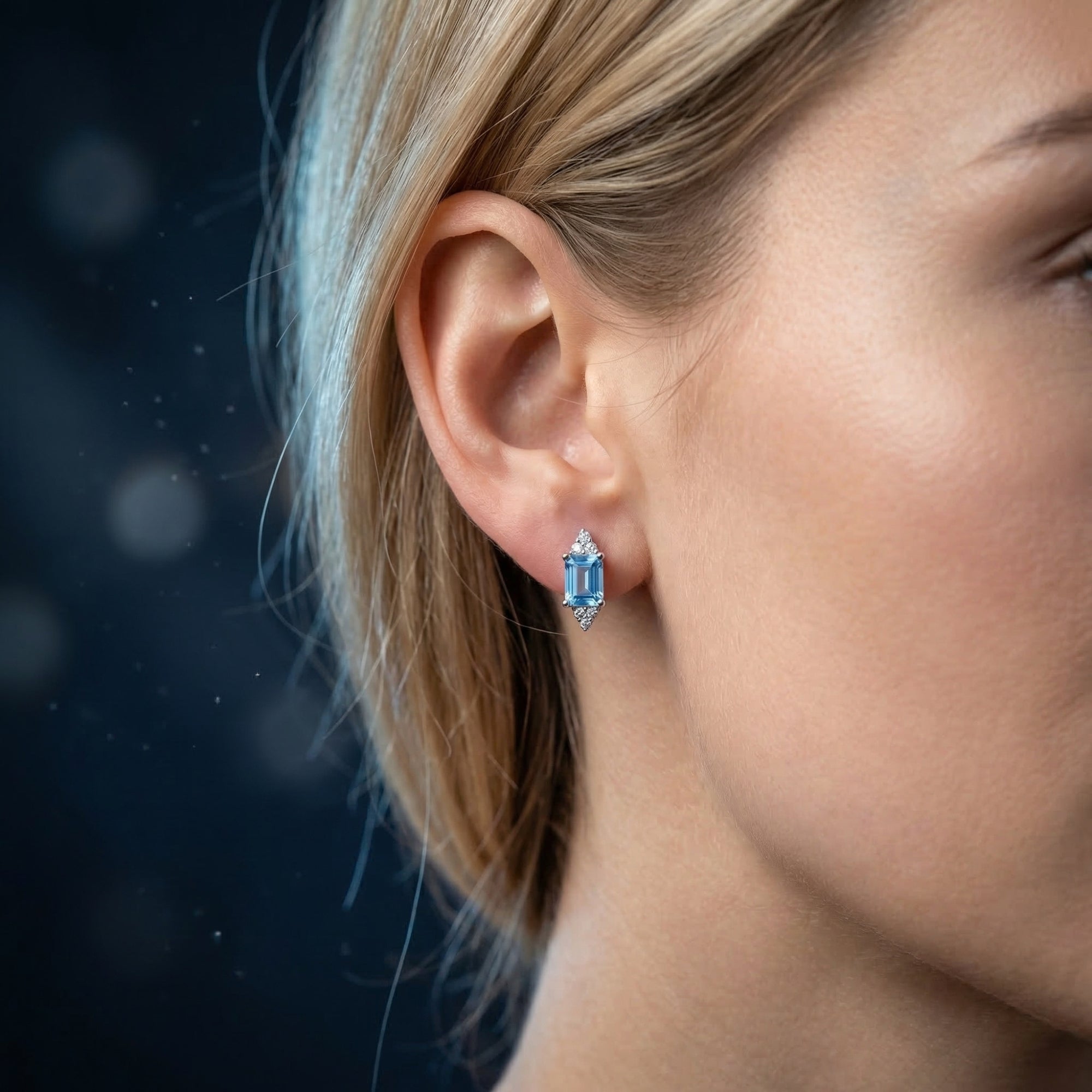 Woman wearing a silver emerald cut natural topaz drop earring with sparkling accents on her ear.