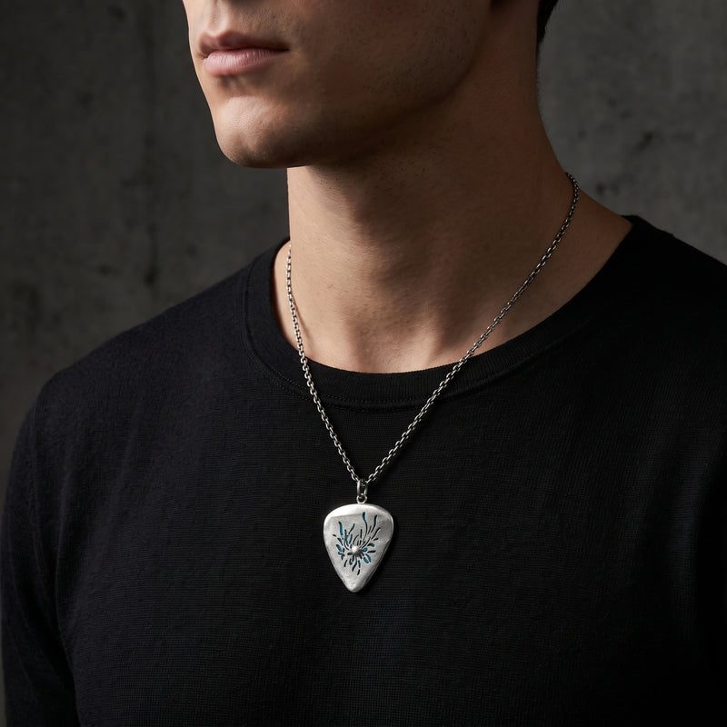 Man wearing the silver guitar-pick pendant necklace over a black crewneck shirt at mid-chest.