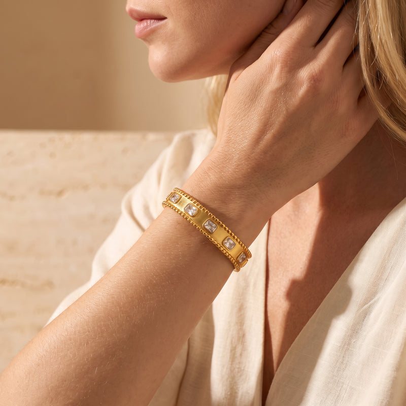 Close-up of a model wearing the gold-tone beaded cuff bracelet with clear bezel-set stones on her wrist.