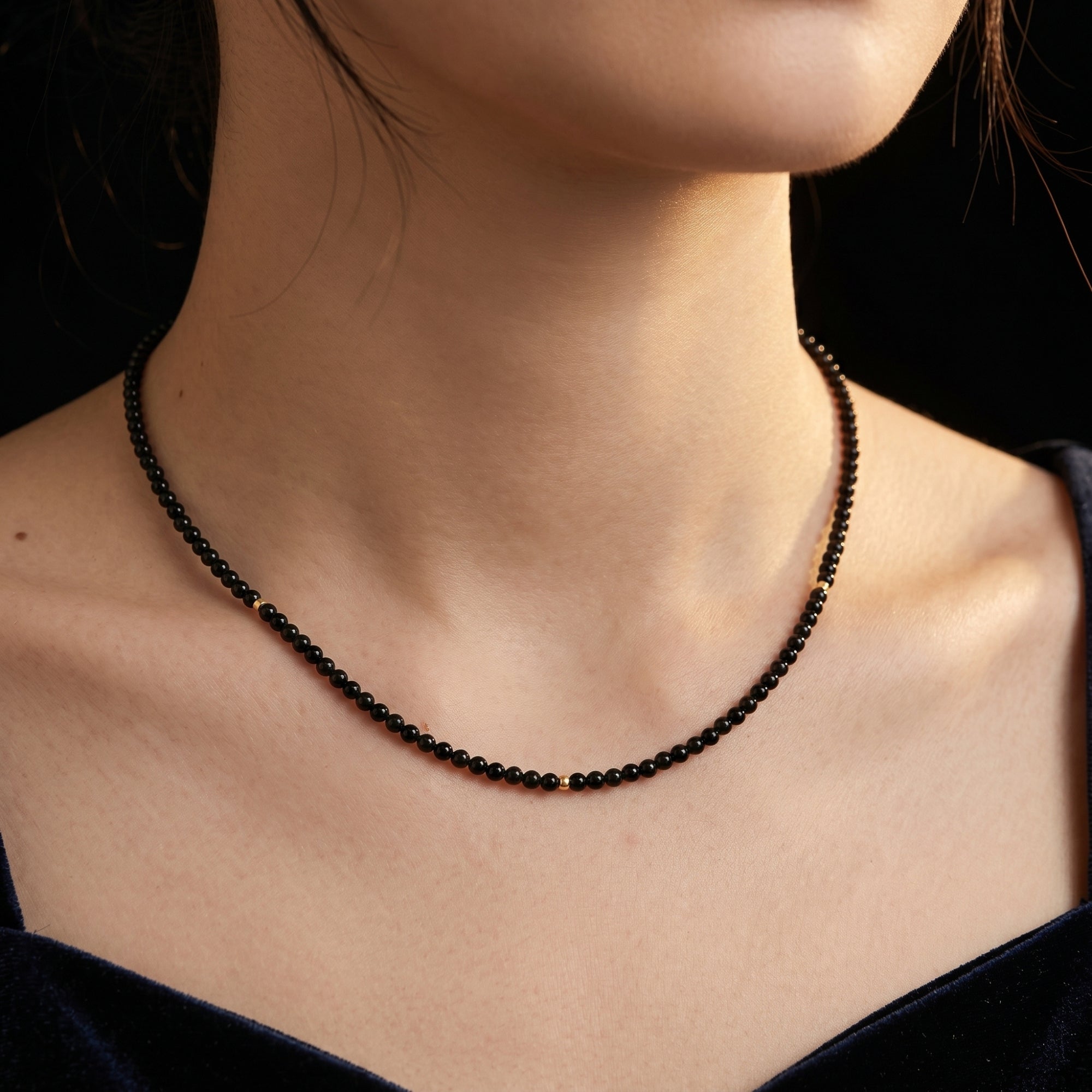 Close-up of a woman wearing the 3mm polished black onyx bead necklace with 18K gold accents against a dark background.