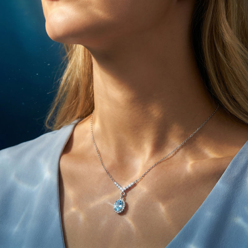 Model wearing the Lyrissa oval aquamarine halo necklace in white gold with a V-shaped diamond-accented chain.