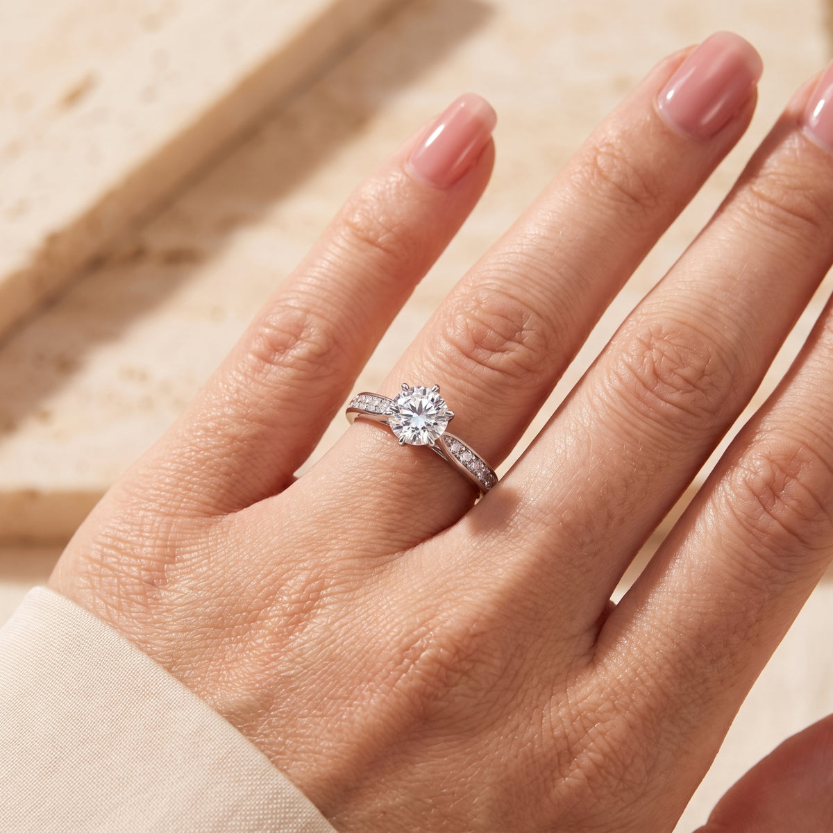 Silver solitaire ring with a round clear center stone and pavé accents worn on a hand's ring finger.