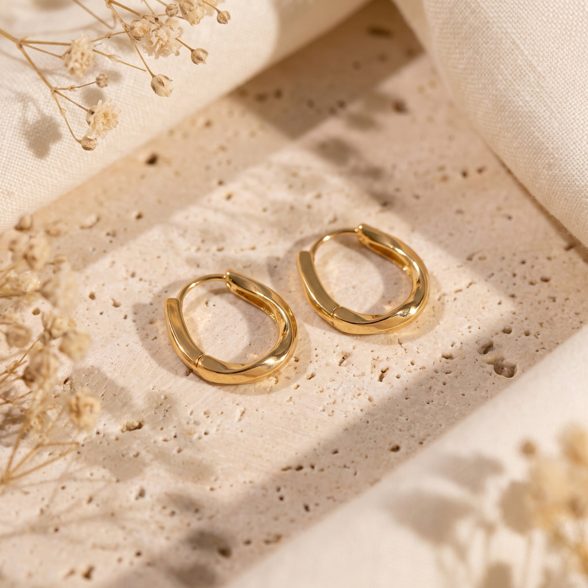 Pair of gold-toned twisted hoop earrings lying flat on a textured beige surface in an overhead view.