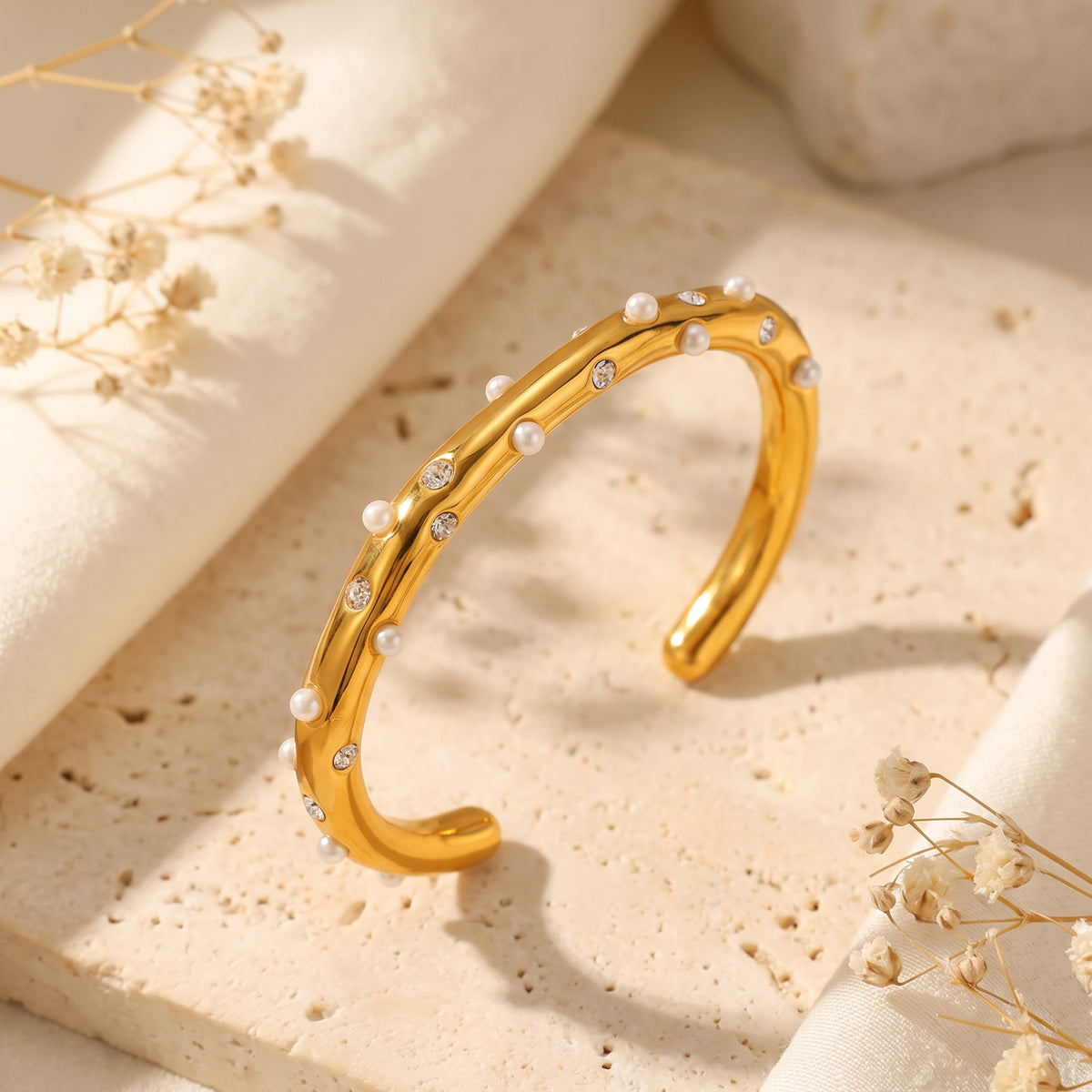 Upright three-quarter view of a gold-tone open cuff bracelet with scattered white pearls and cubic zirconia accents.