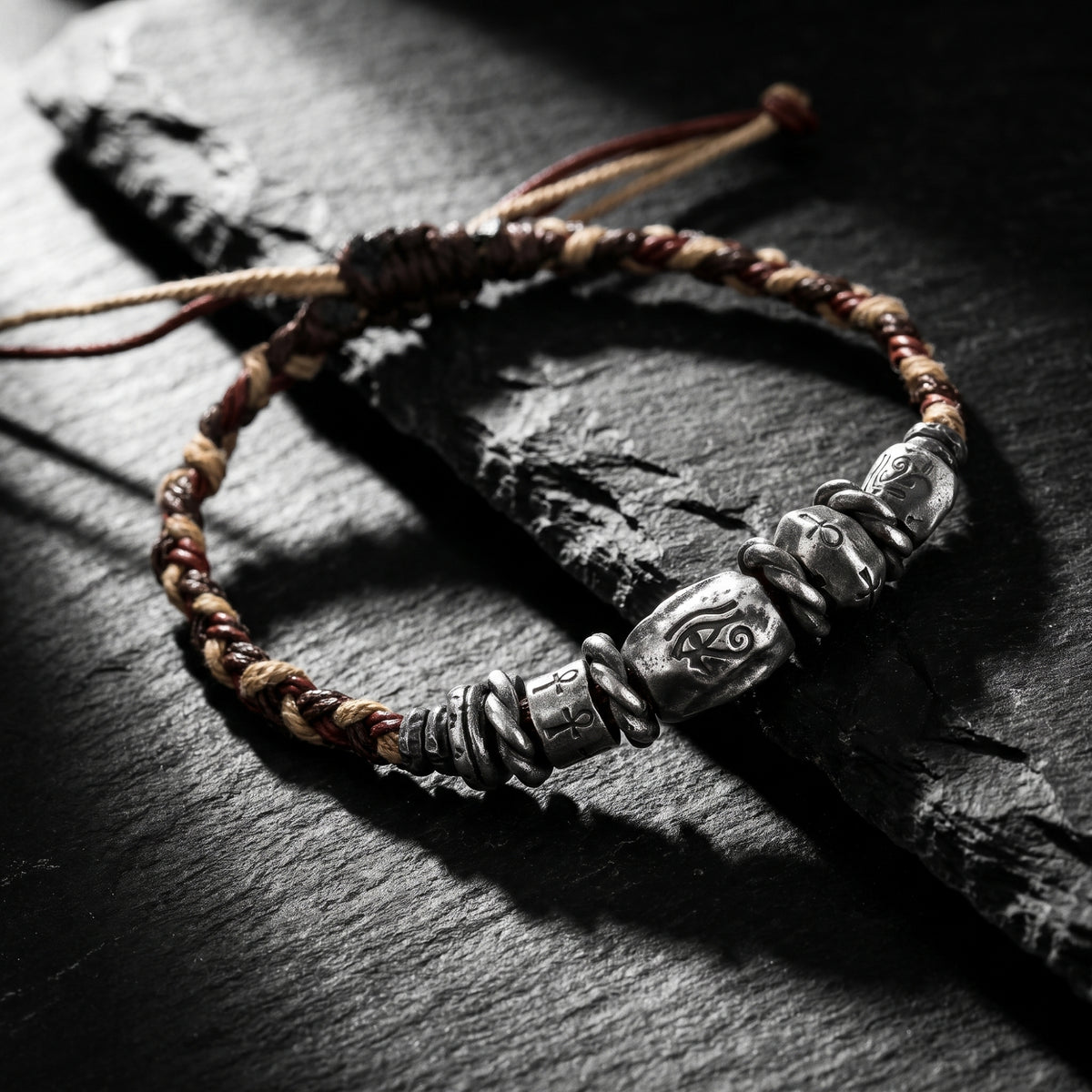 Angled close-up of the Eye of Horus braided bracelet with silver beads on black slate.