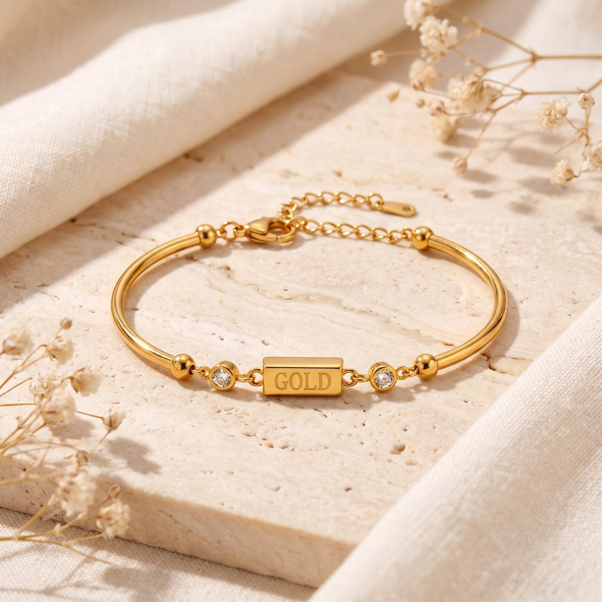 Gold-tone bar bracelet laid flat, showing its lobster clasp and extension chain on a stone surface.