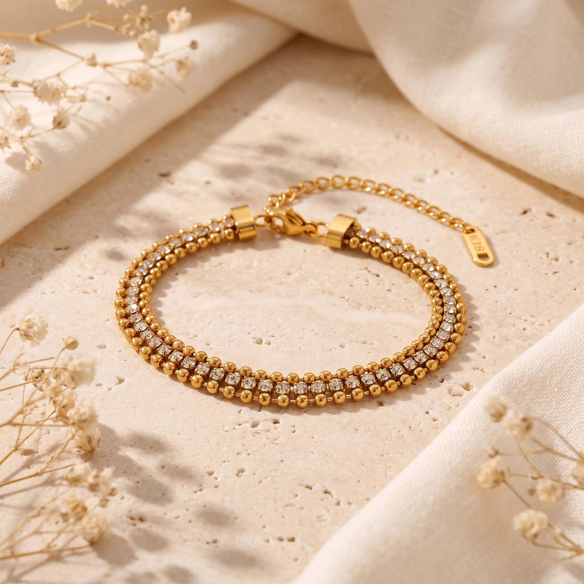 Angled view of a gold-tone triple-row beaded bracelet with cubic zirconia laid on a stone surface.