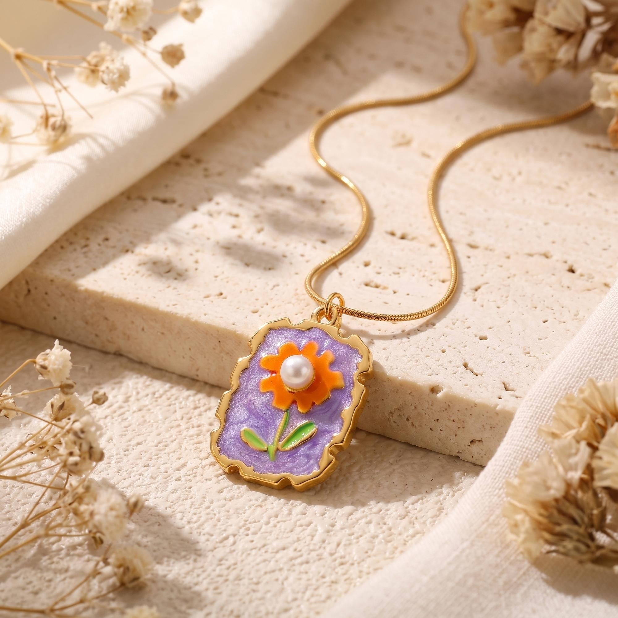 Detailed view of the gold floral pendant with purple enamel, orange flower, and a white simulated pearl core.