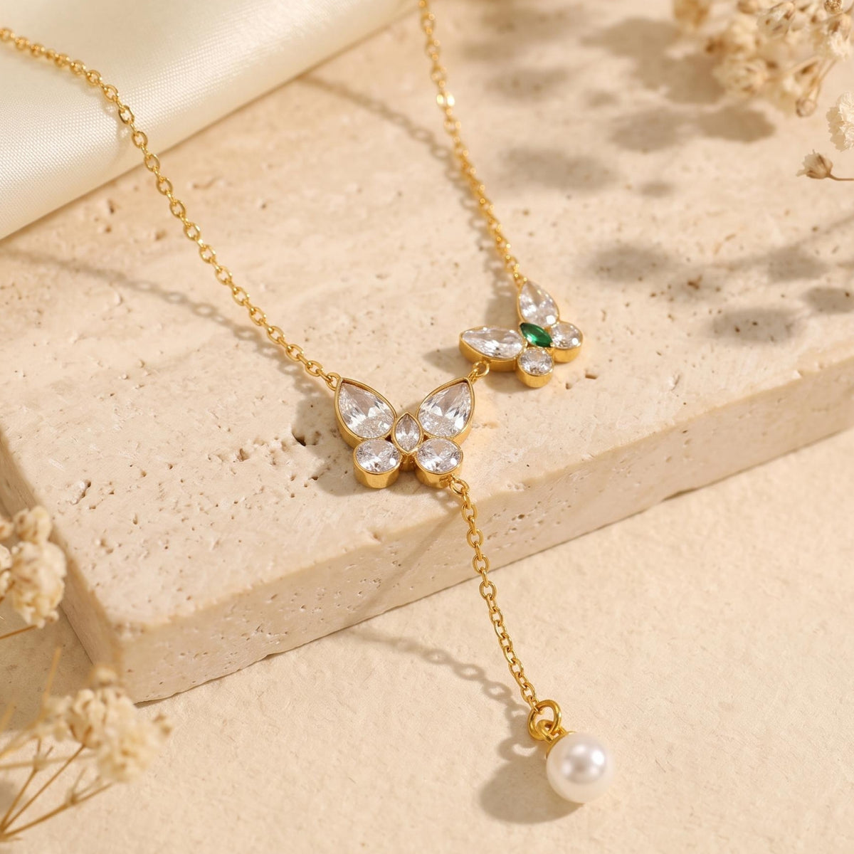 Close-up of a gold-tone necklace with two crystal butterfly pendants, green accents, and a pearl drop.