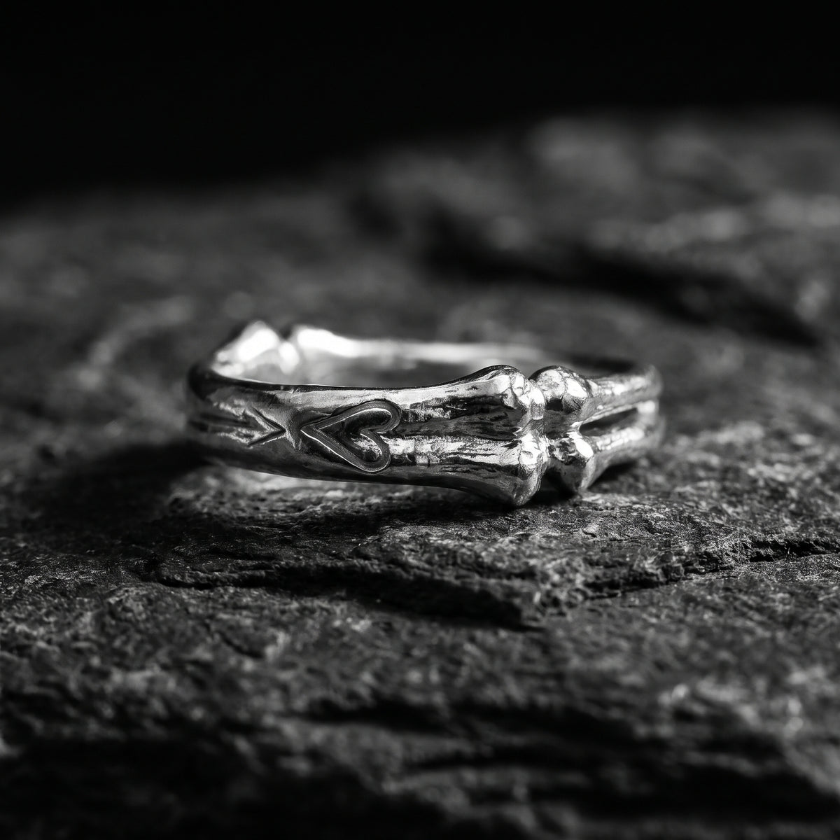 Side view of the silver bone-motif open band ring lying horizontally on black stone, with its heart detail visible.