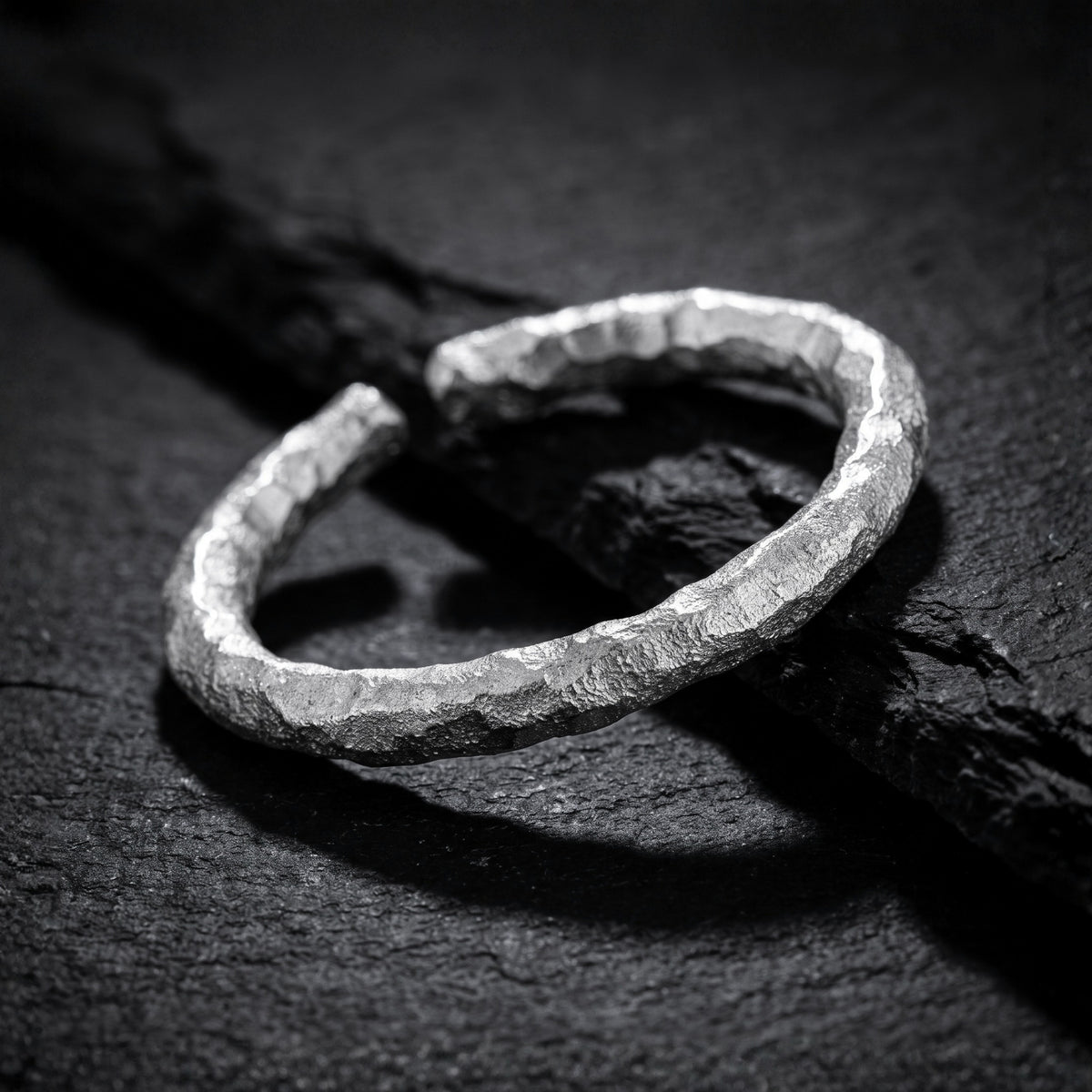 Angled close-up of the chiseled open ring resting on a dark textured slab, with its open gap visible.