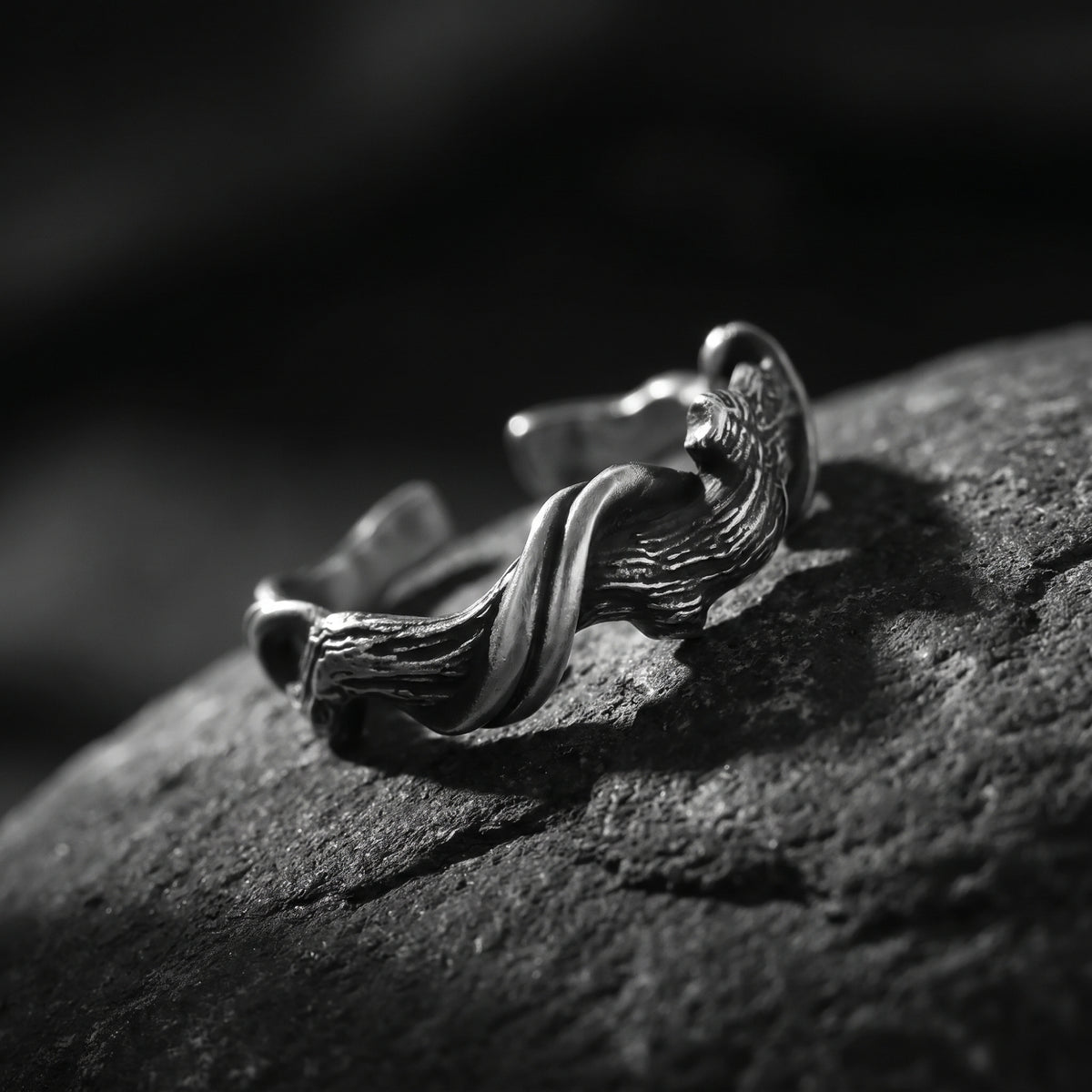 Angled close-up of the silver open band ring with organic wood-grain texture on a dark stone surface.