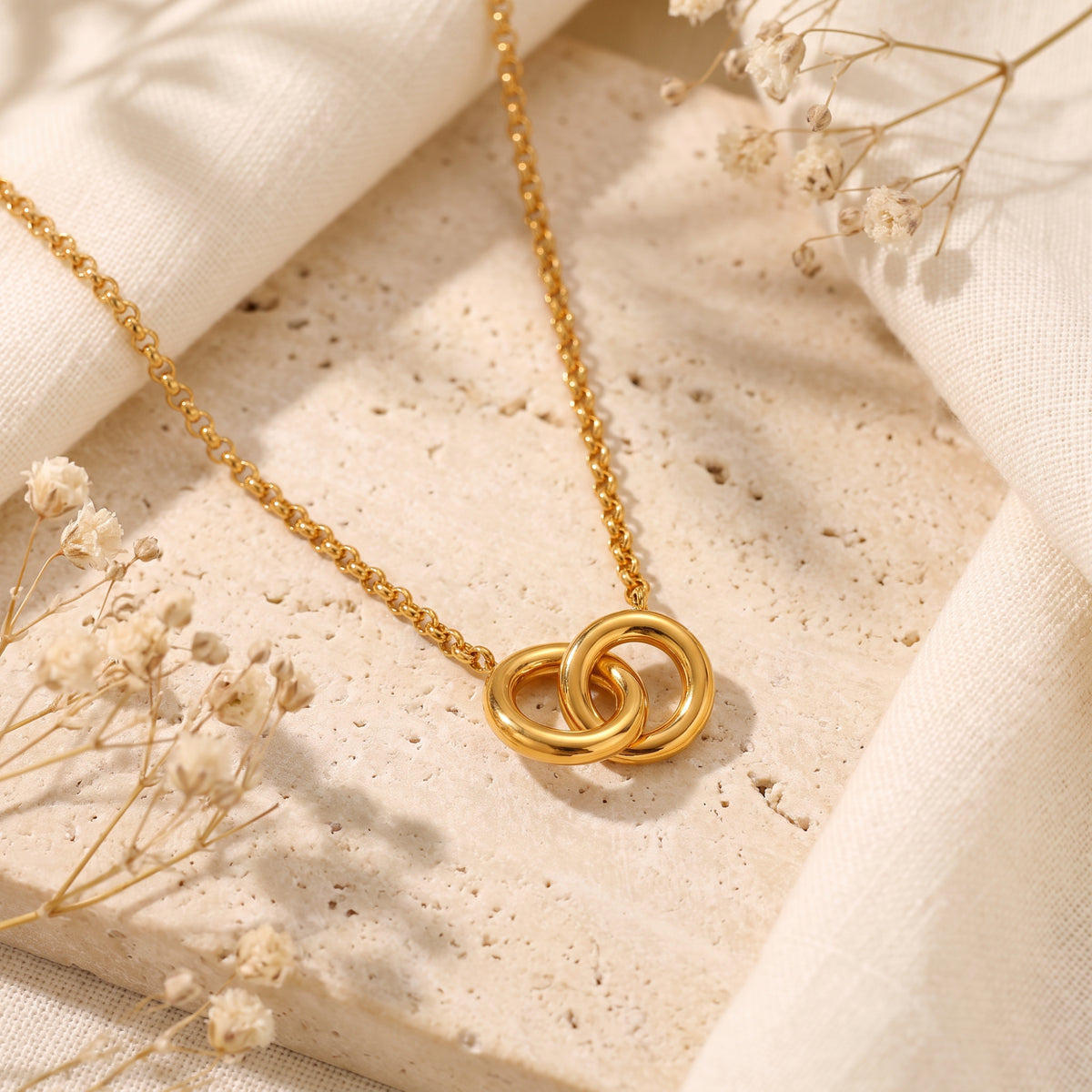 Flat-lay view of the gold-tone interlocking circle pendant necklace resting on textured stone and beige linen.
