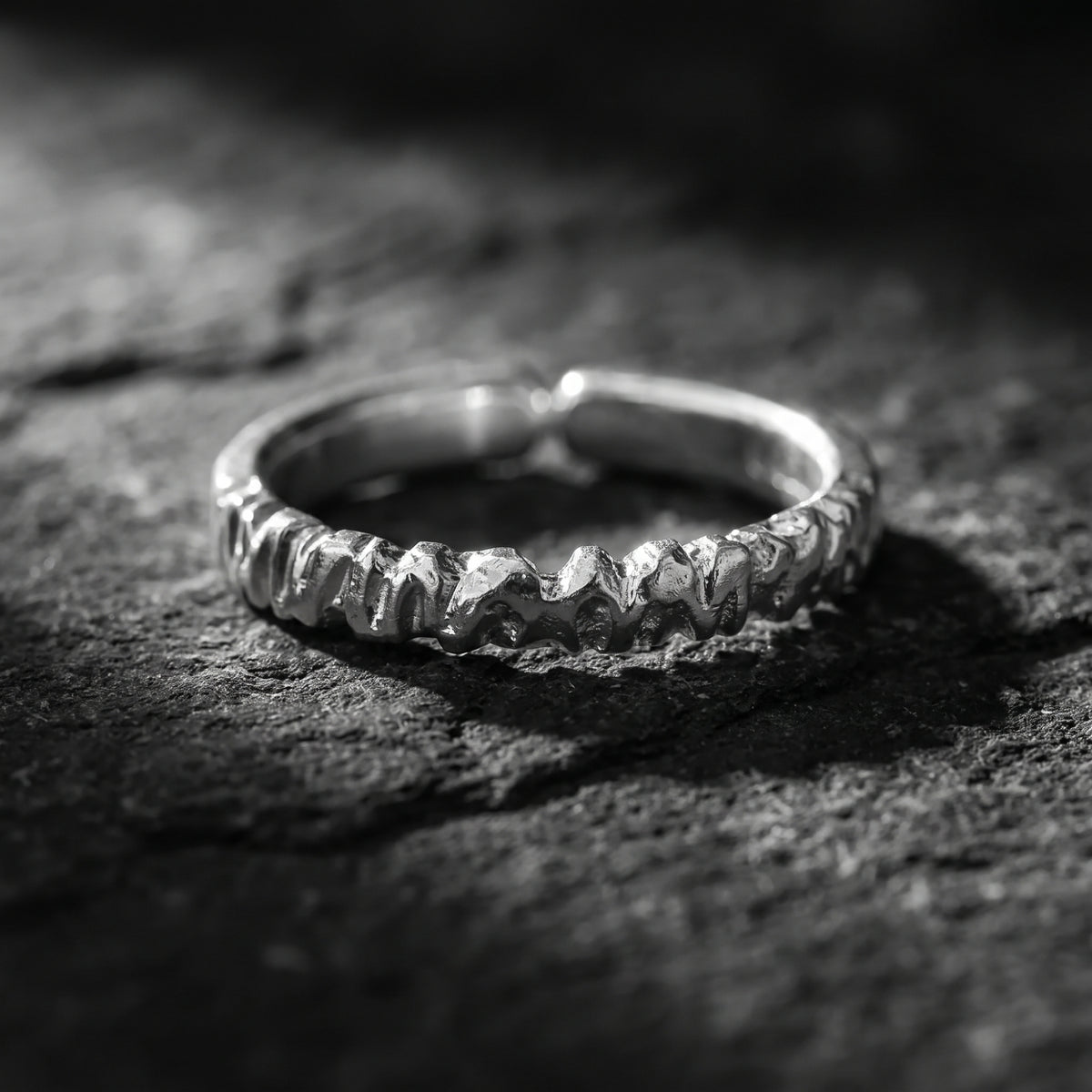 Carved silver ring resting flat on dark stone, displaying its open-band gap.