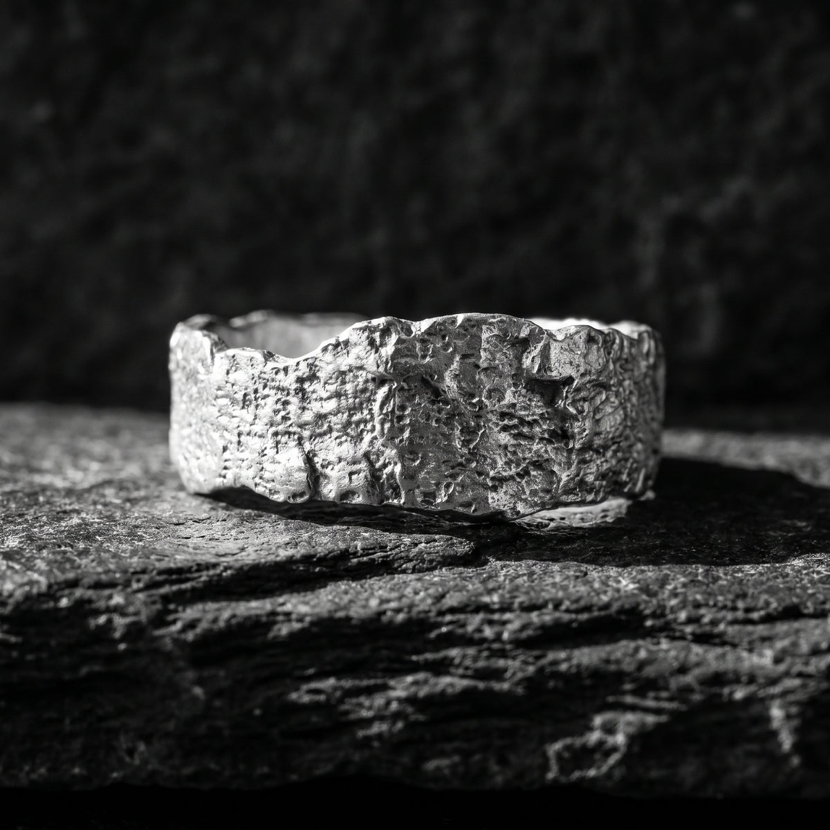 Front profile view of the heavily textured raw silver band ring resting on dark stone.