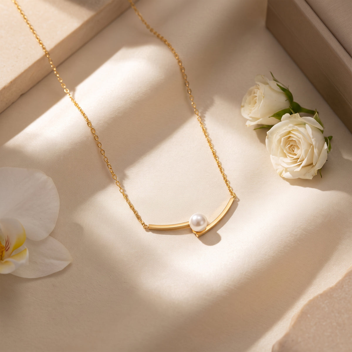 Gold-tone arc pearl necklace laid on cream silk beside white roses and an orchid