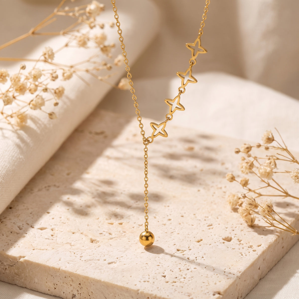 Gold-tone lariat necklace displayed on a pale stone slab, with four openwork star stations and a long bead drop.