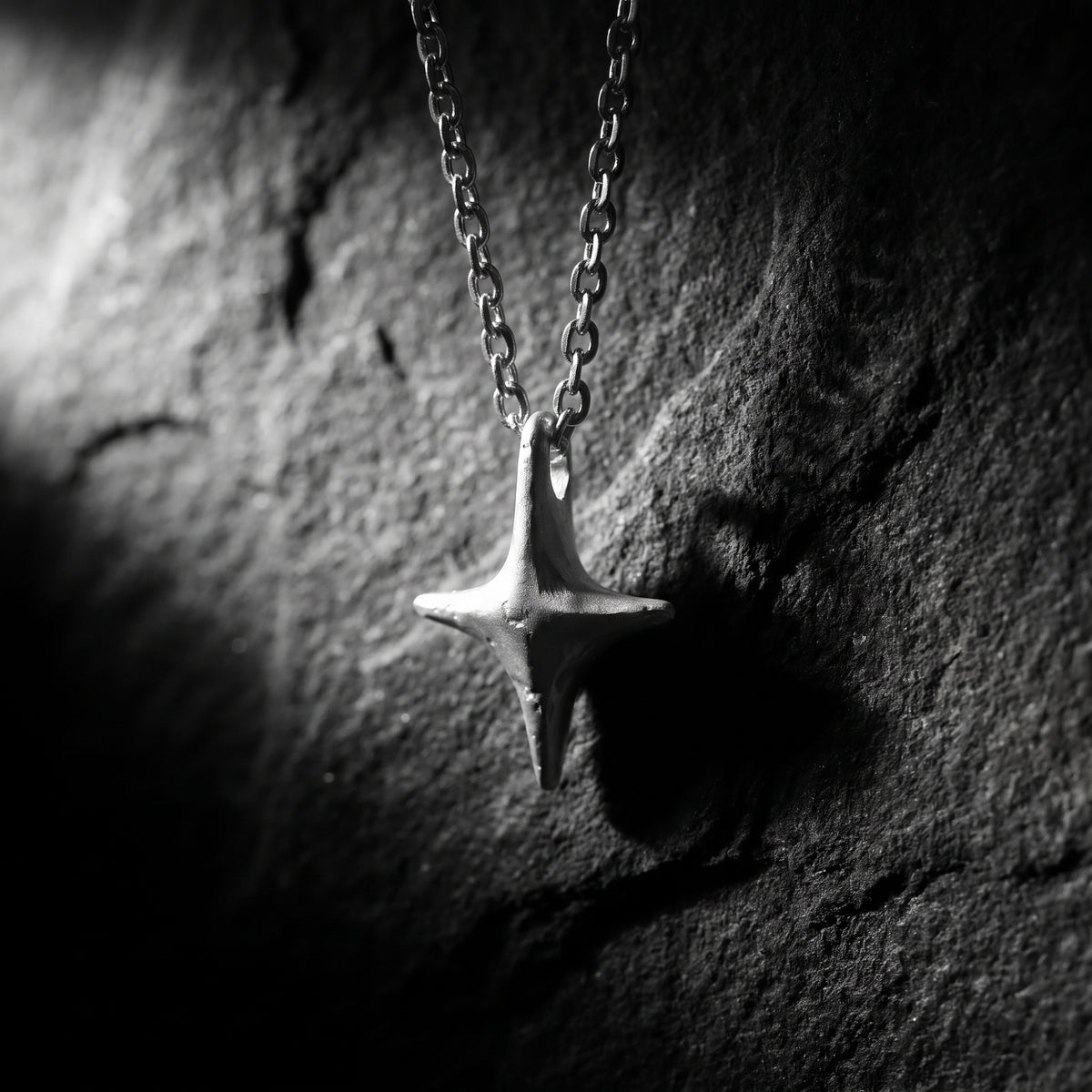Close-up of a silver four-point starburst pendant hanging from a chain against a dark textured backdrop.