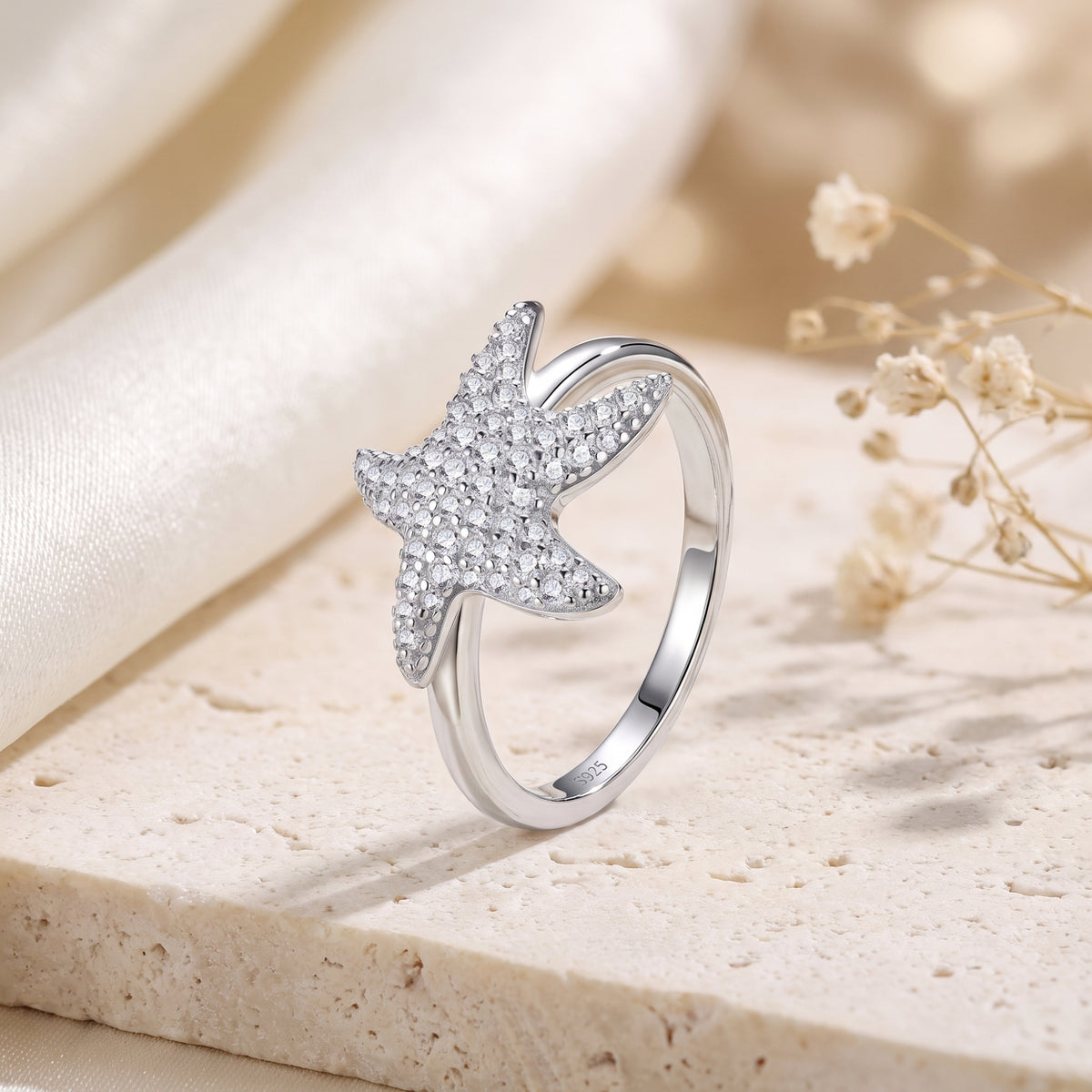 Upright silver starfish ring on a stone slab, showing its pave-set stones and inner band marked S925.