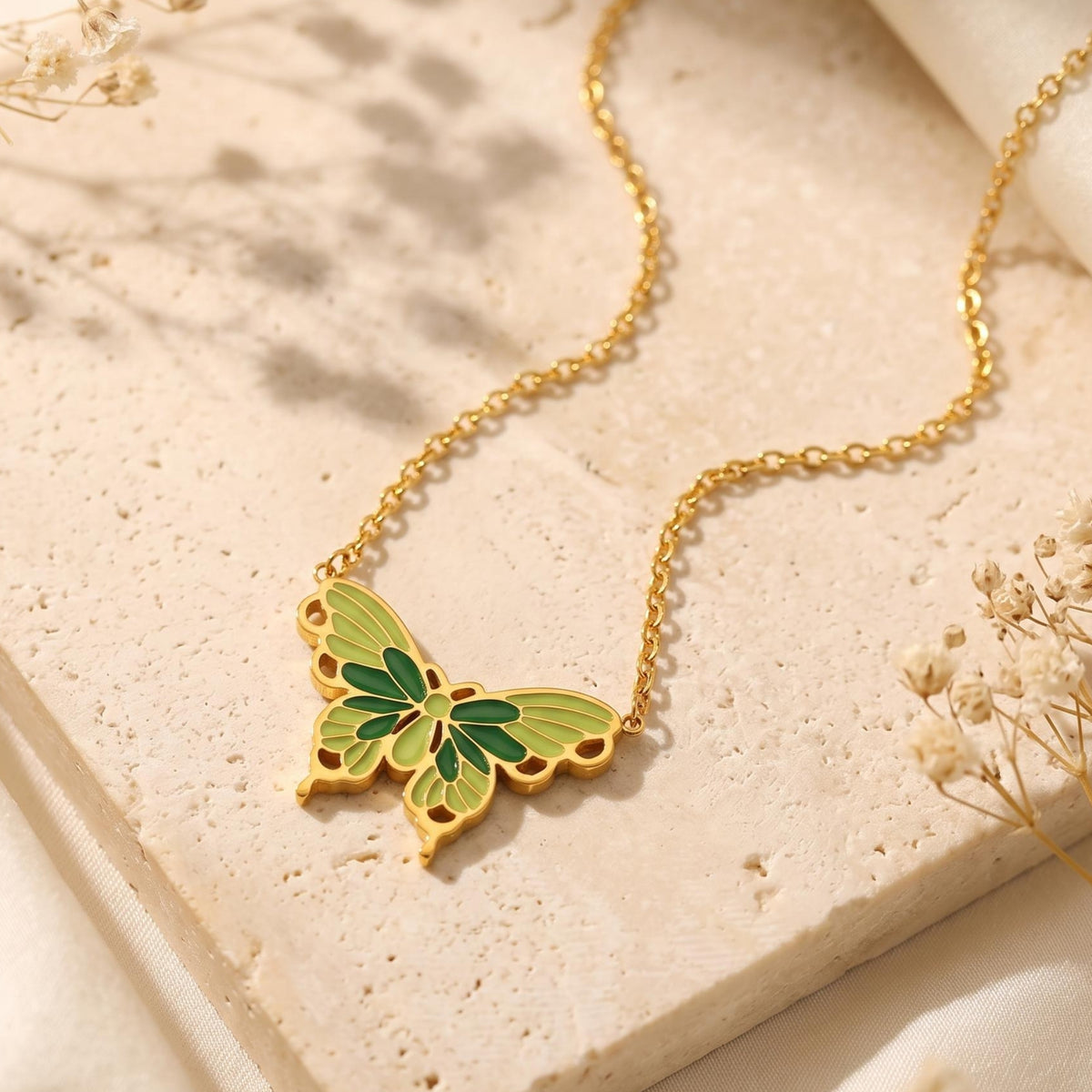 Top-down view of a gold-tone butterfly pendant necklace with green and olive enamel on a stone slab.