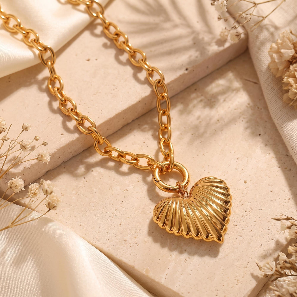 Close-up flat lay of the gold-tone ribbed heart pendant and link chain on a stone slab.