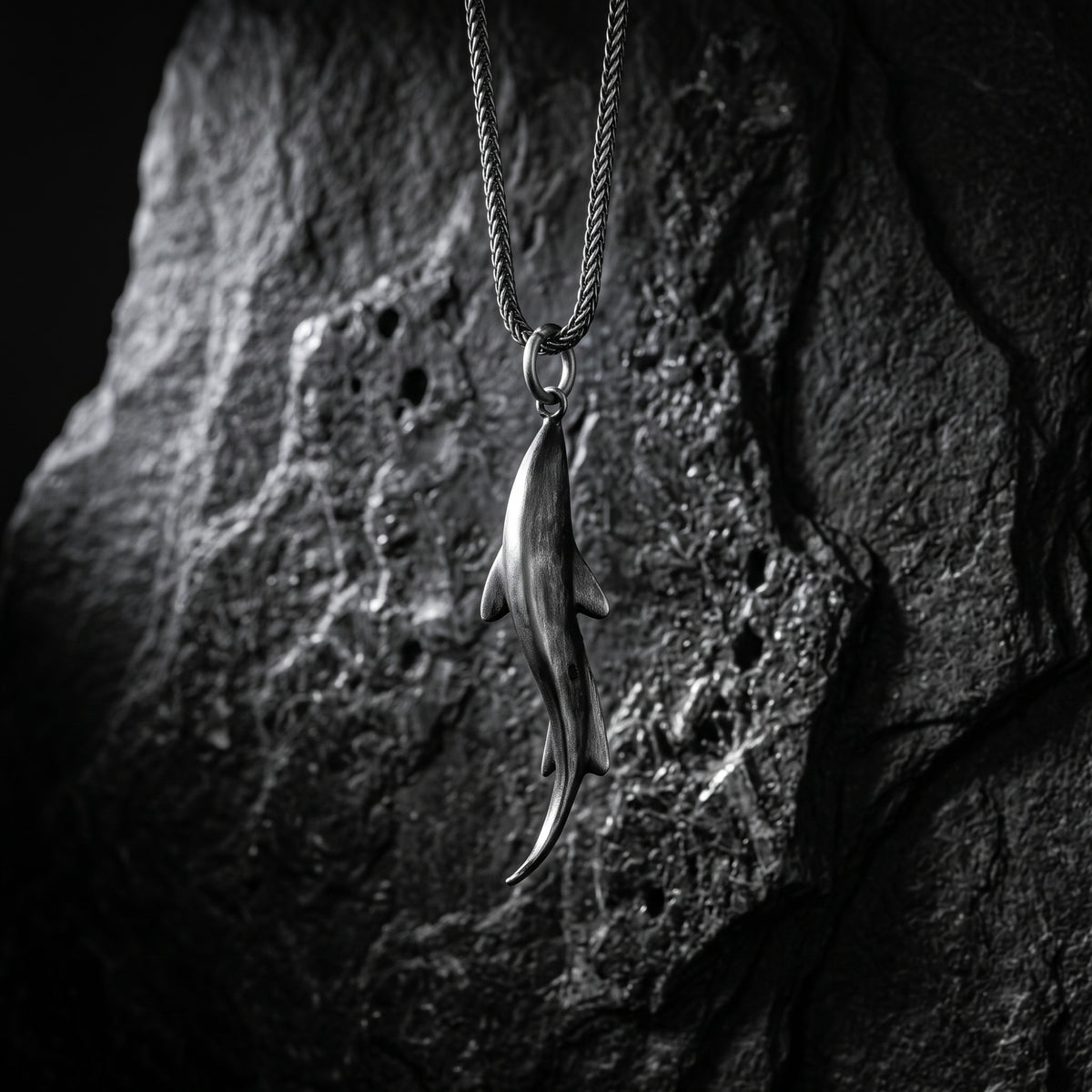 Silver shark pendant hanging vertically against a rough dark stone background