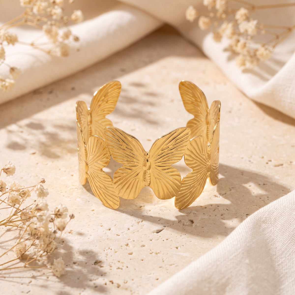 Upright gold-tone open cuff bracelet with ridged butterfly wings displayed on a light stone surface.