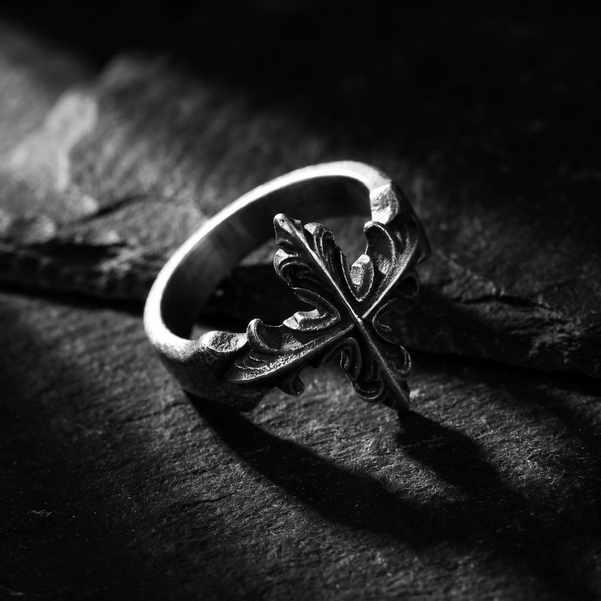 Angled close-up of the silver open ring showing its curved band and ornate cross on dark rock.