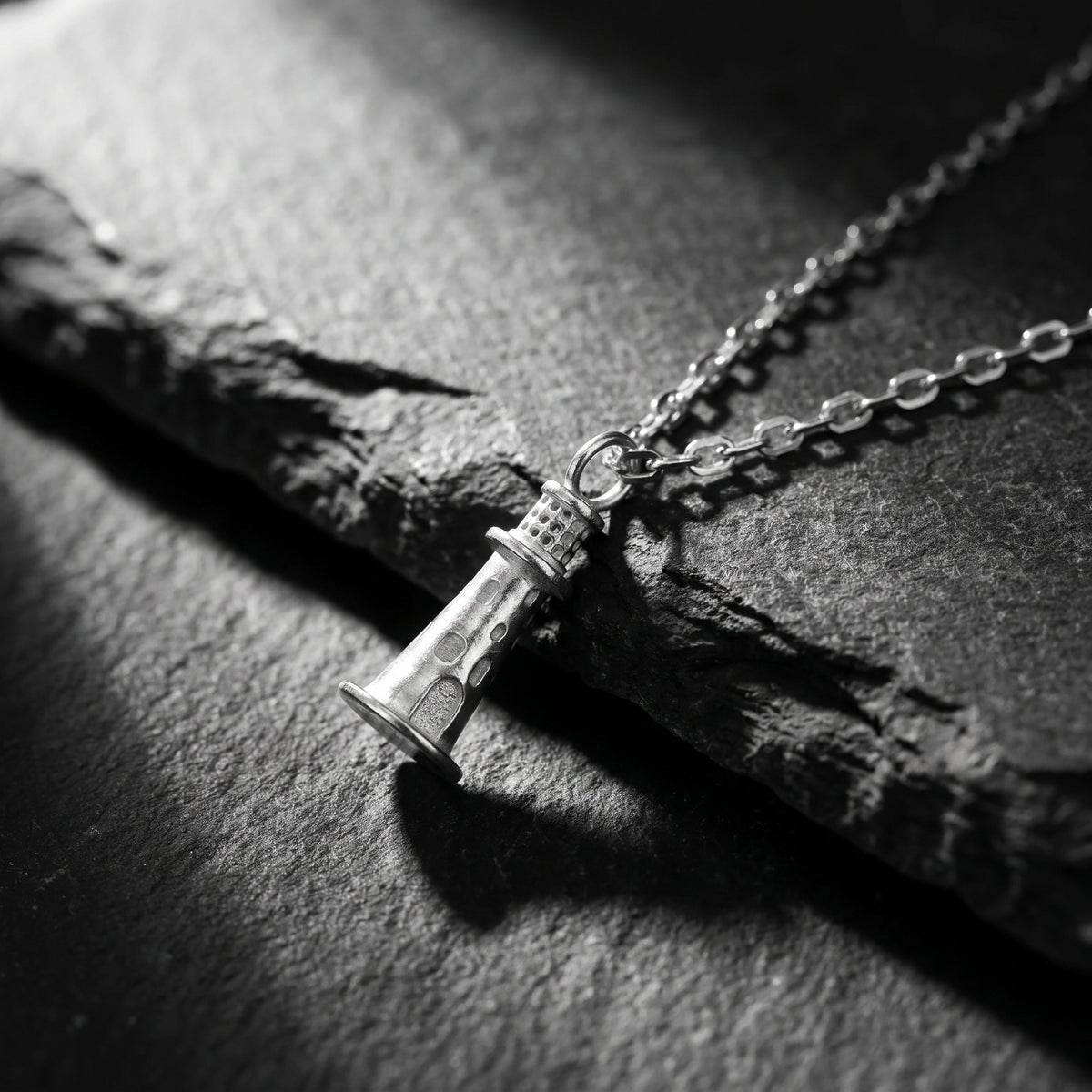 Angled close-up of the silver lighthouse pendant and chain resting on dark slate.