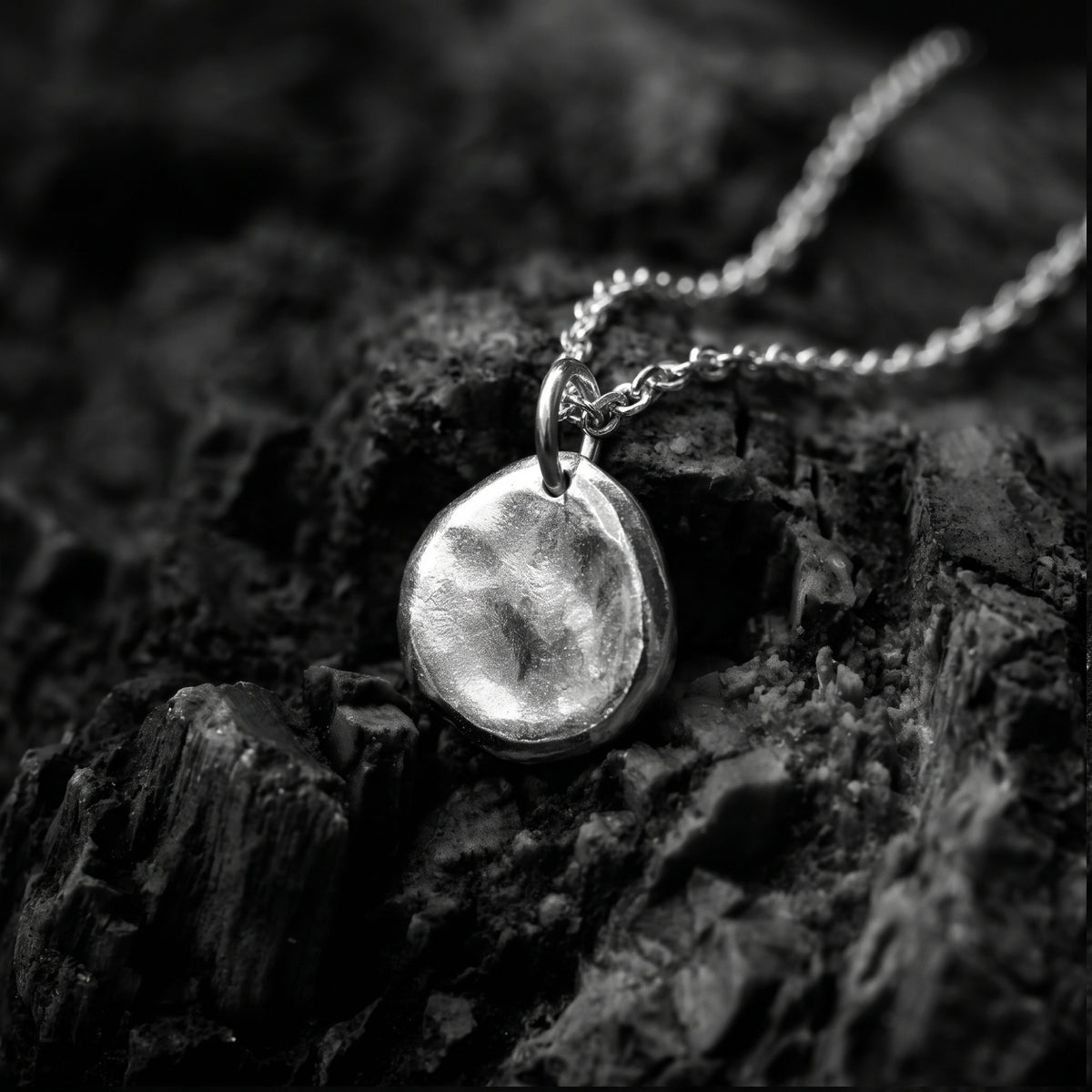 Angled close-up view of the silver textured pebble pendant resting on dark rough rock.