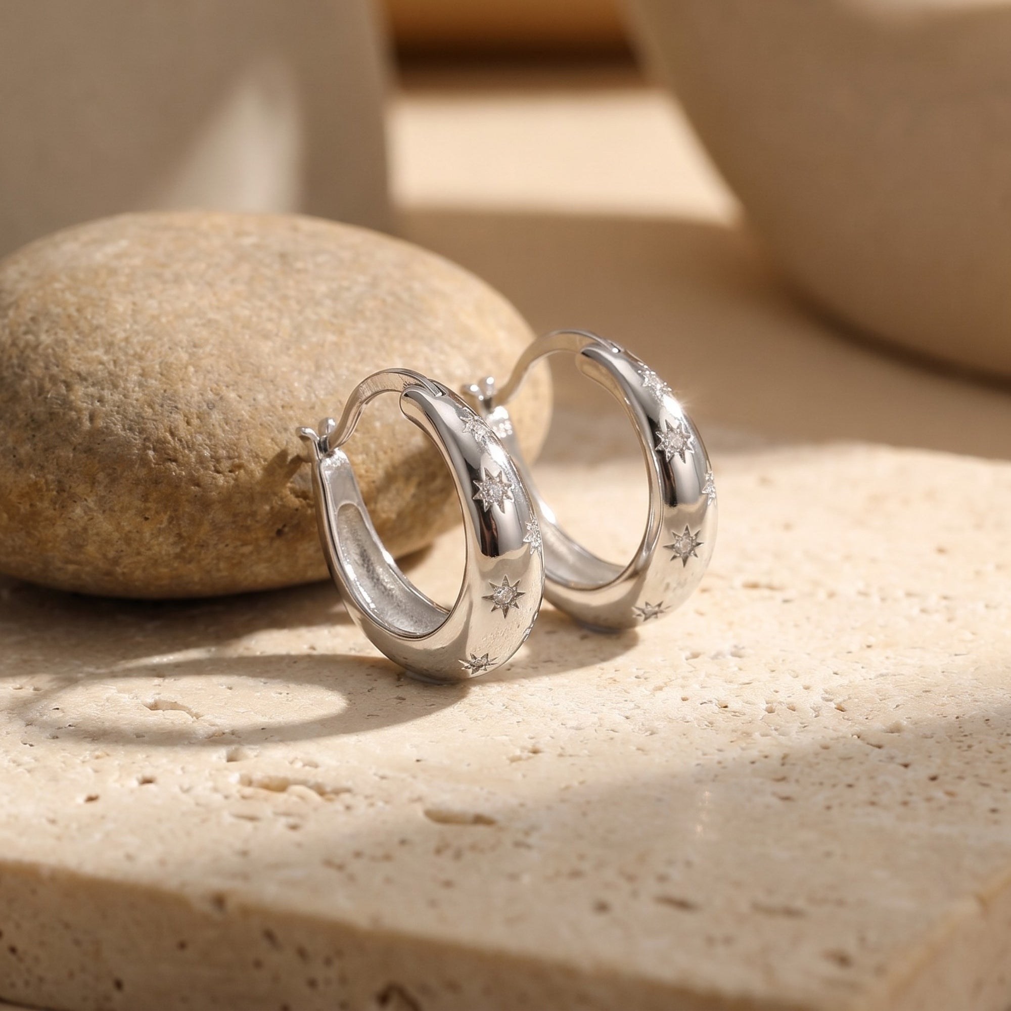 Sterling silver starburst huggie hoop earrings with simulated diamond accents on a neutral stone background.