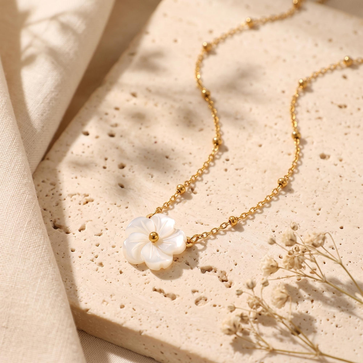 High-angle view of the gold-tone bead-station necklace and carved white flower pendant on a pale textured stone surface.