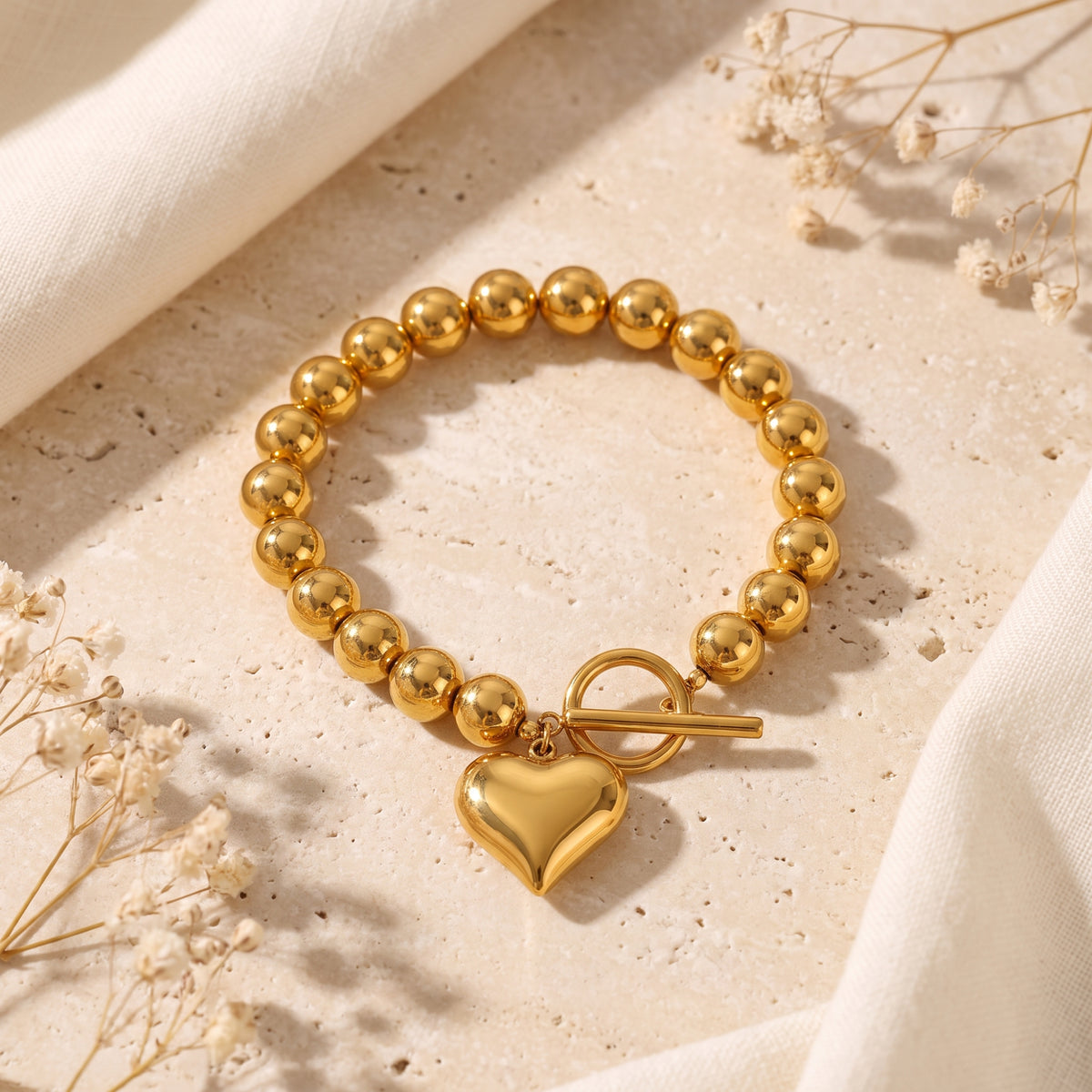 Full view of the gold-colored beaded toggle bracelet with a heart charm laid flat on a stone background.