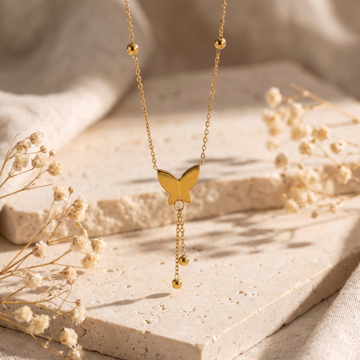 Gold-tone butterfly lariat necklace suspended vertically over a textured stone surface.