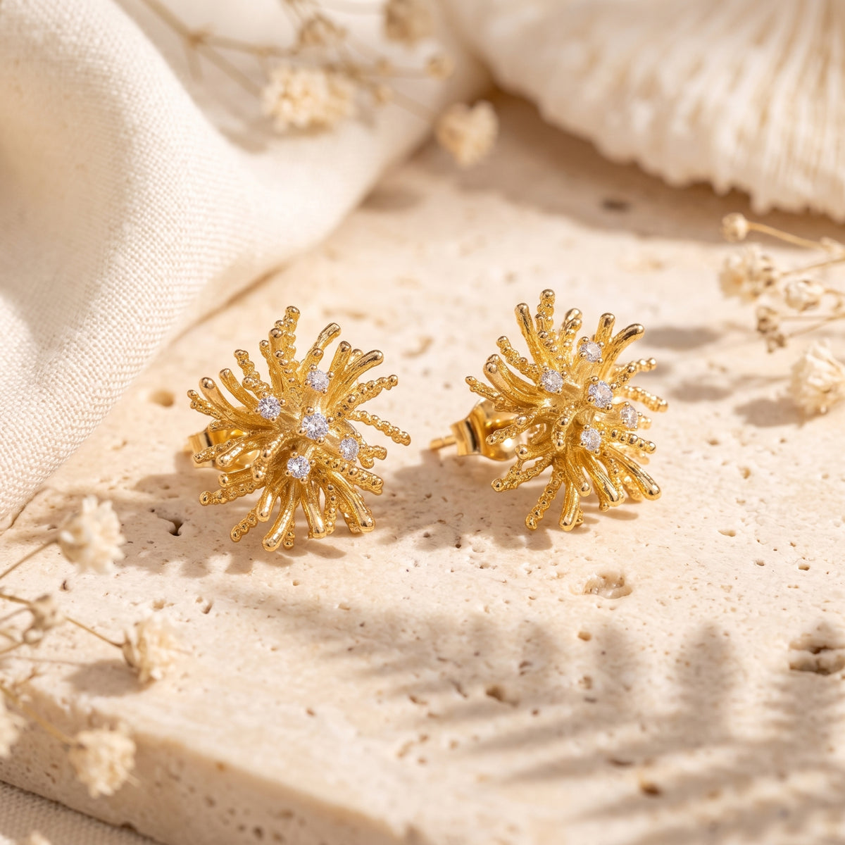 Pair of gold-tone starburst stud earrings angled on textured stone, showing post backs and clear stones.