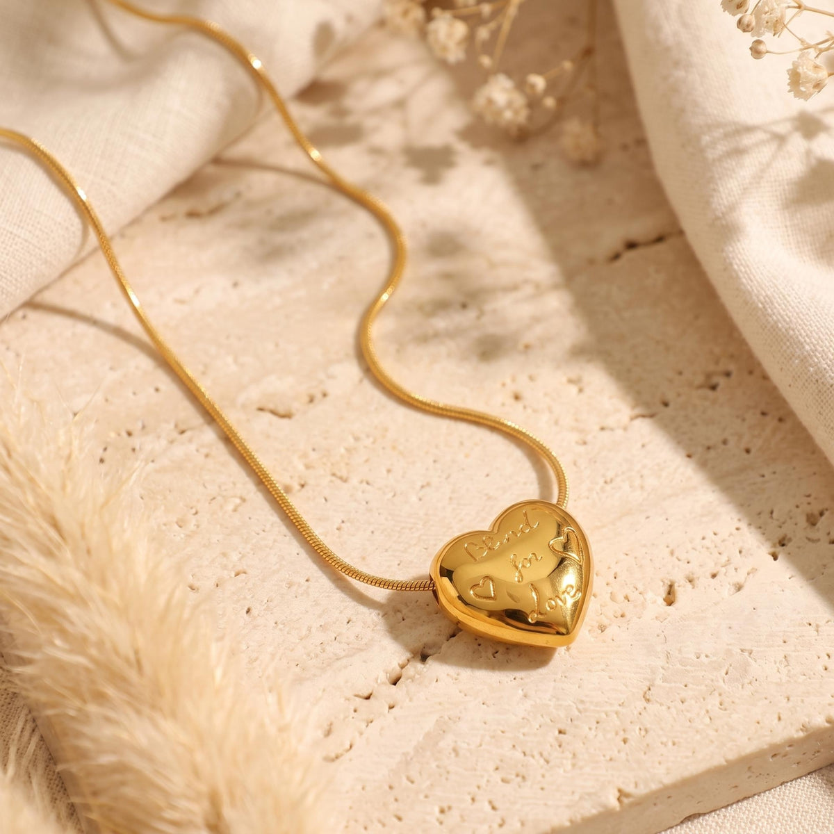 Angled view of the gold-tone engraved heart necklace laid on a light textured stone slab.