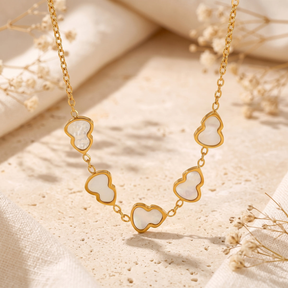Close-up of a gold station necklace suspended over stone, showing five mother-of-pearl gourd charms.