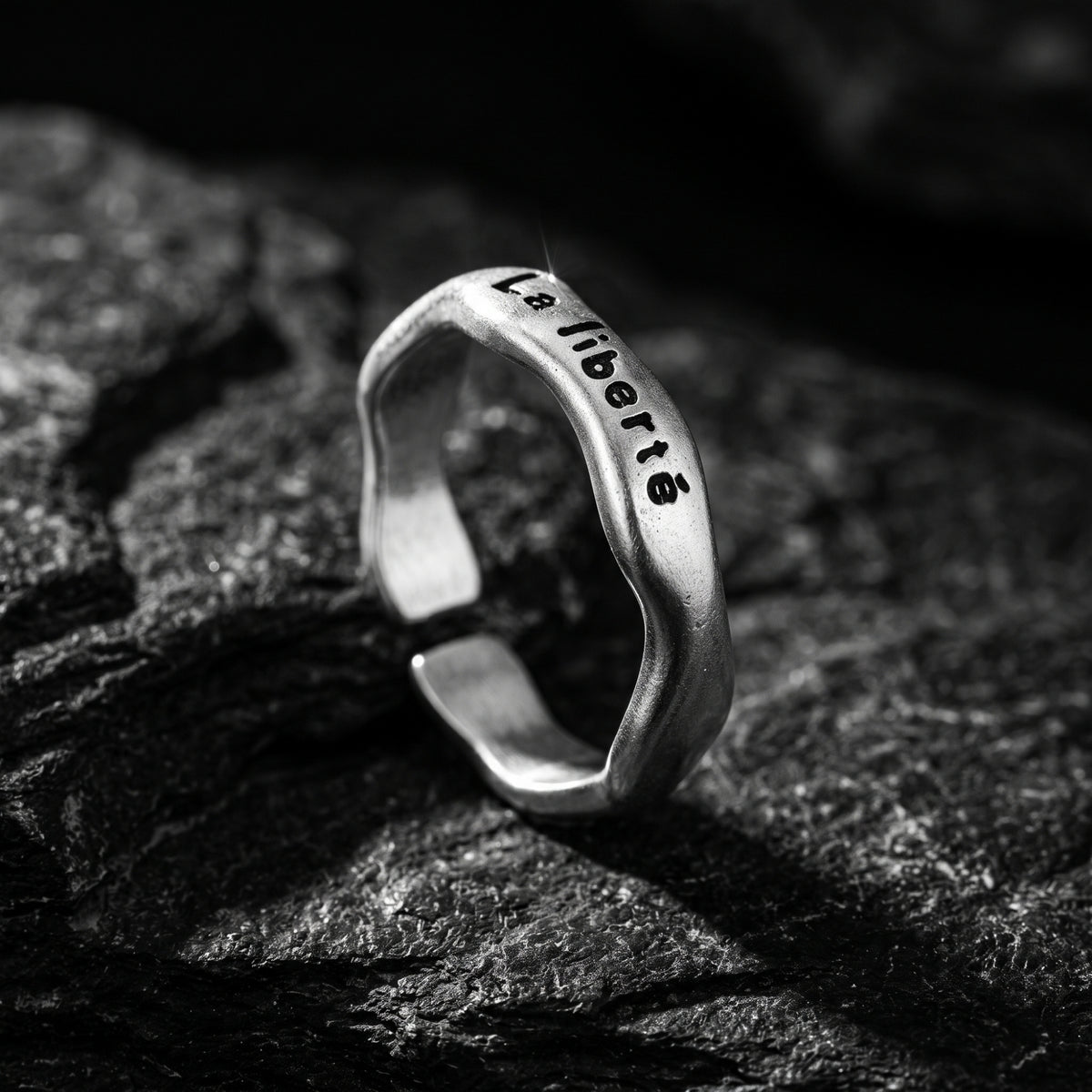 Three-quarter view of the engraved open band ring standing upright on dark slate.