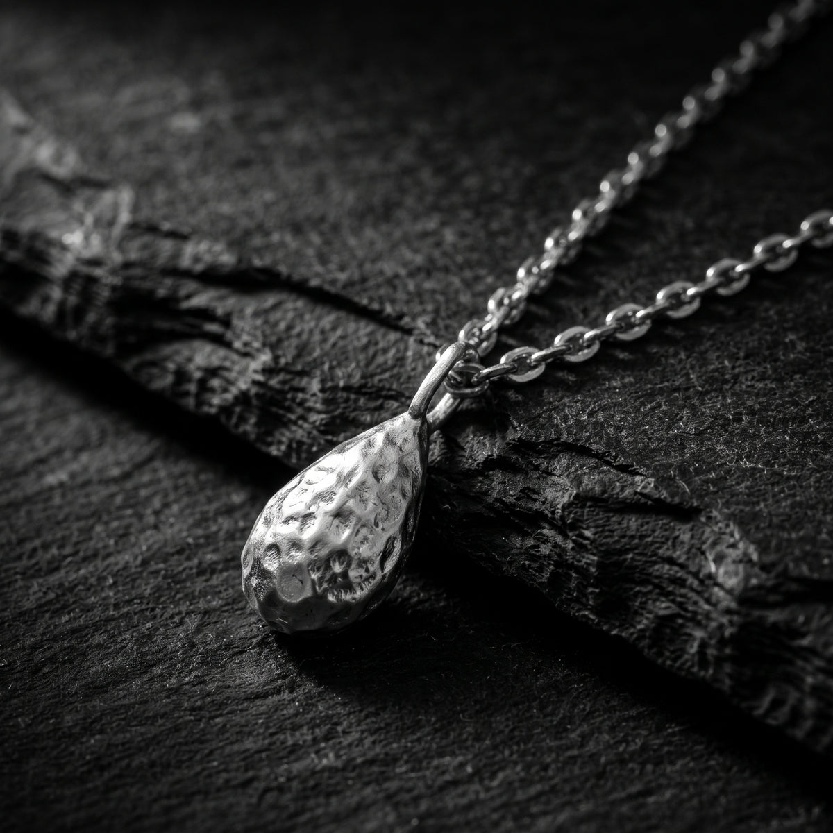 Close-up of the textured silver teardrop pendant and chain lying on a dark slate surface.