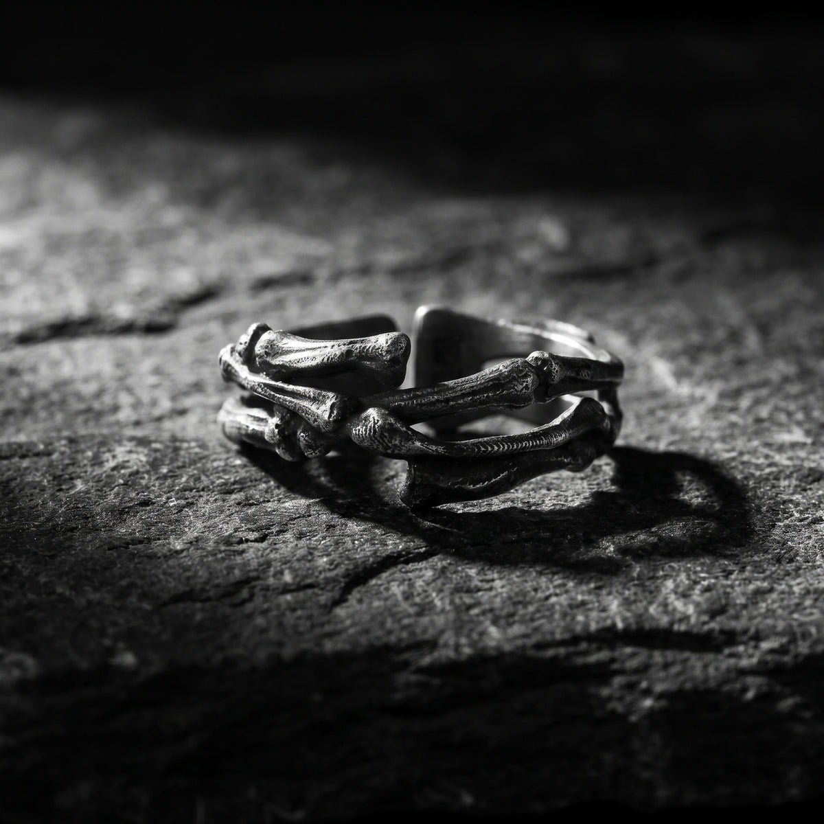 Angled view of the silver skeletal open band ring showing overlapping sculpted bone-like forms on textured dark rock.