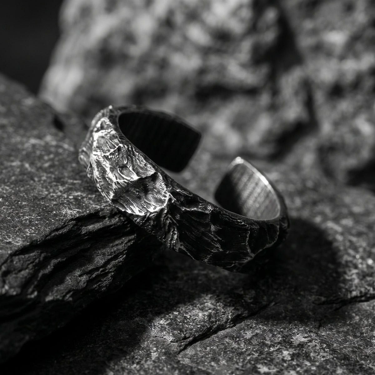 Angled macro view of the silver open ring on dark slate, showing its textured exterior and open gap.