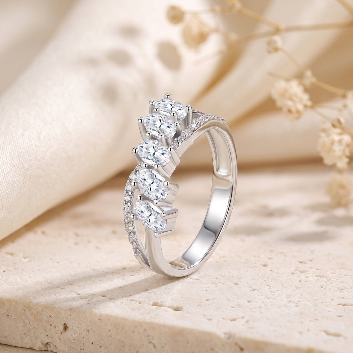 Side view of a silver bypass ring with five prong-set oval stones and pavé accents along the split band.