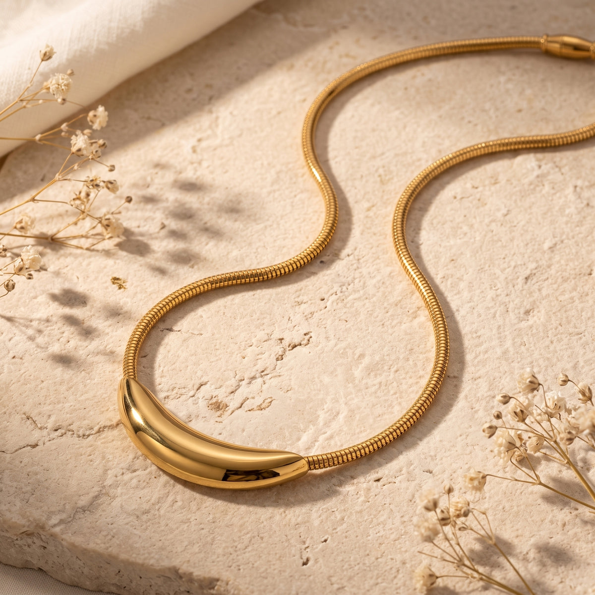Flat lay of the gold-tone curved crescent collar necklace laid flat on a textured stone slab.