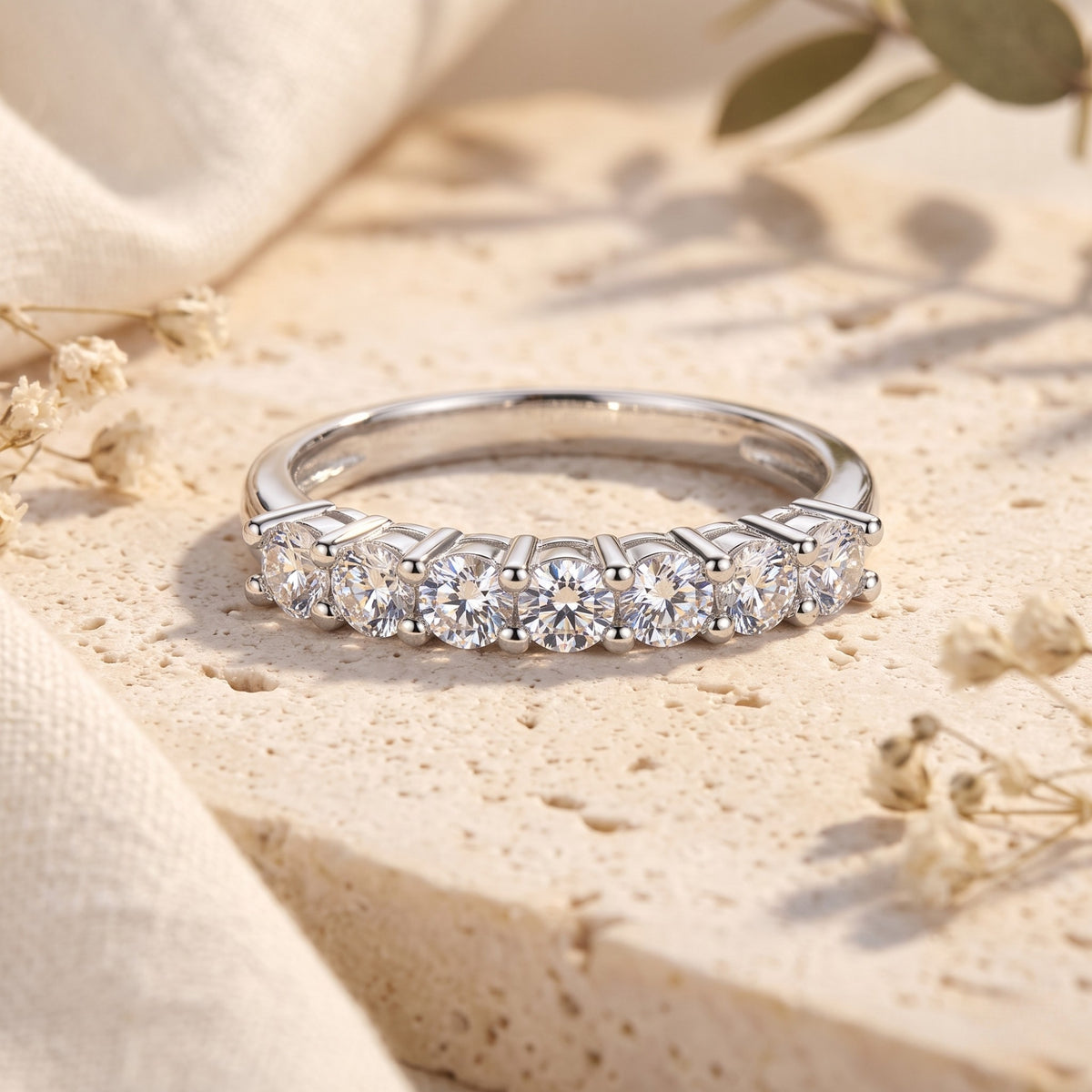 Front-facing view of the silver band ring with seven round clear stones on a textured beige stone.